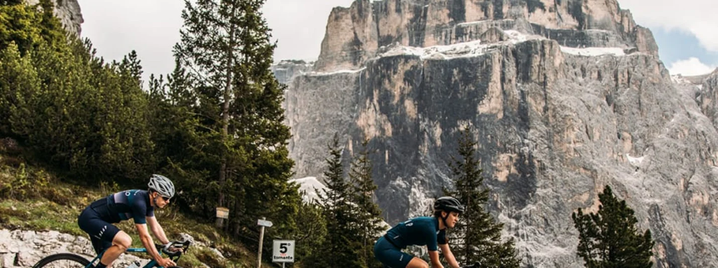 Switchback Short Stay - 3 nights Due ciclisti pedalano su strada di montagna con scogliera rocciosa e pini sullo sfondo
