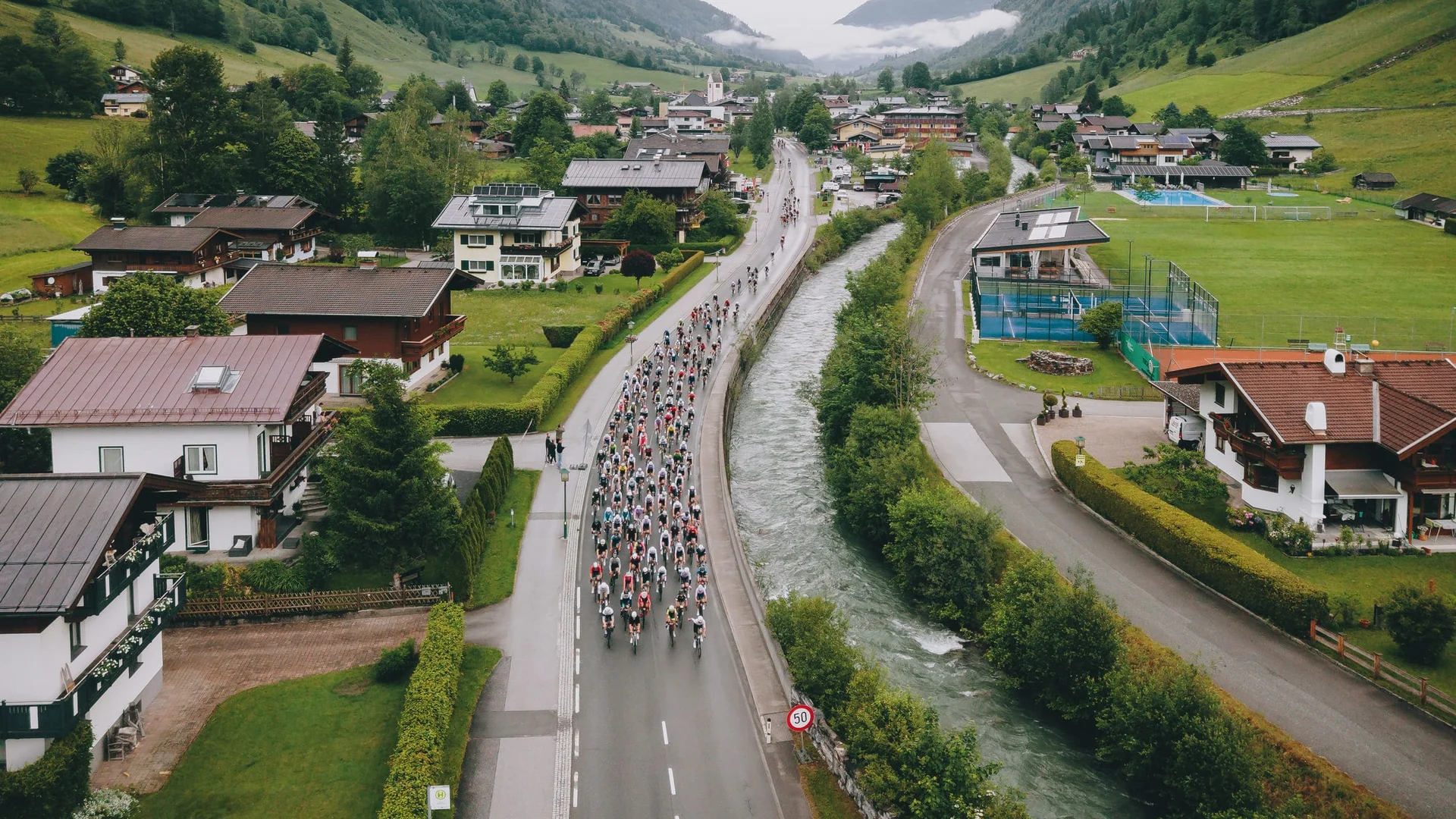 Glocknerkönig 2026 © BRUCK FUSCH GROSSGLOCKNER JFK Photography Fahrradrennen durch ein malerisches Bergdorf mit Fluss und Häusern