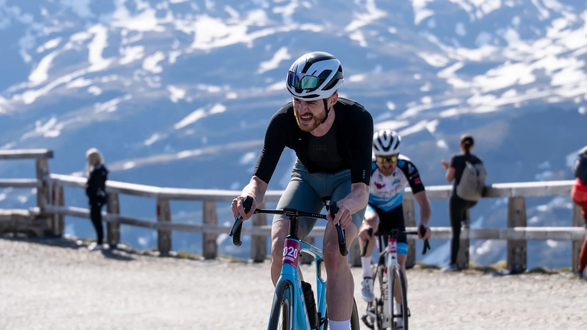 Cyclist climbing cobblestone mountain road with snowy peaks in background