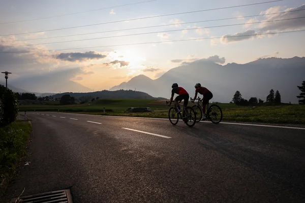 Österreich © Felix Saller Zwei Radfahrer fahren auf einer Straße bei Sonnenuntergang in den Bergen