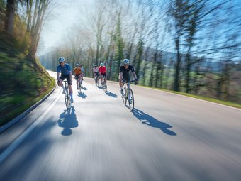 Gruppe von Radfahrern fährt schnell auf einer Straße im Wald bei Sonnenschein