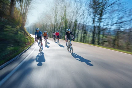 Gruppo di ciclisti che pedala velocemente su strada nel bosco al sole