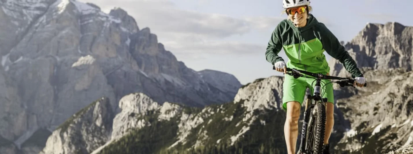 Ciclista con casco in mountain bike su sentiero di montagna con vista alpina