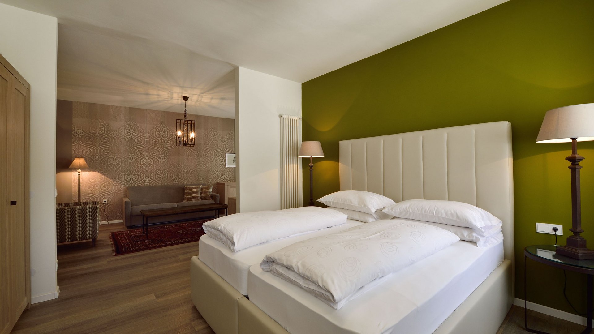 Modernes Schlafzimmer mit Doppelbett, grüner Wand und angrenzendem Wohnzimmer