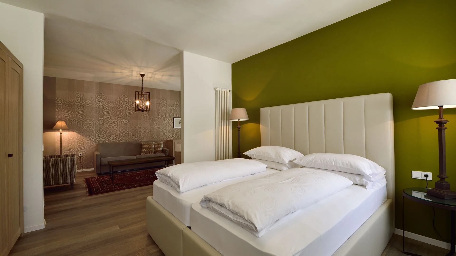 Modern bedroom with double bed, green wall, and adjoining living room
