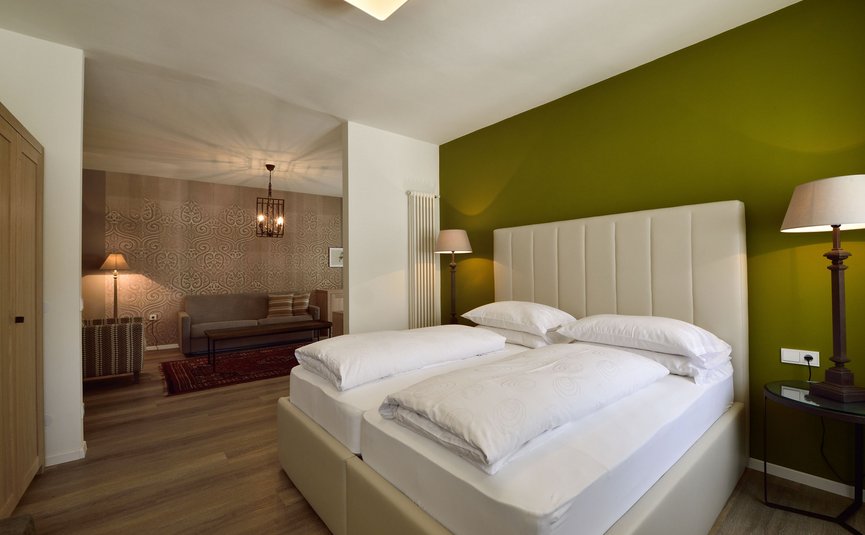 Modernes Schlafzimmer mit Doppelbett, grüner Wand und angrenzendem Wohnzimmer
