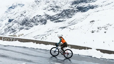 Fahrradfahrerin auf verschneiter Bergstraße mit schneebedecktem Berg im Hintergrund