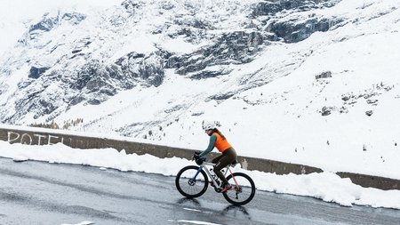 Fahrradfahrerin auf verschneiter Bergstraße mit schneebedecktem Berg im Hintergrund