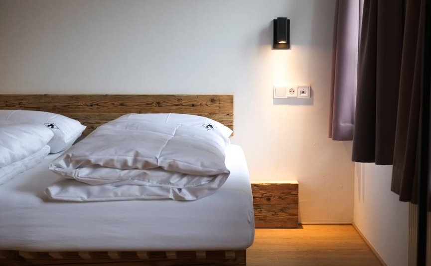 Camera da letto moderna con letto in legno, biancheria bianca e lampada da parete