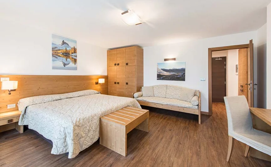 Bright hotel room with double bed, sofa, wooden furniture, and wall art