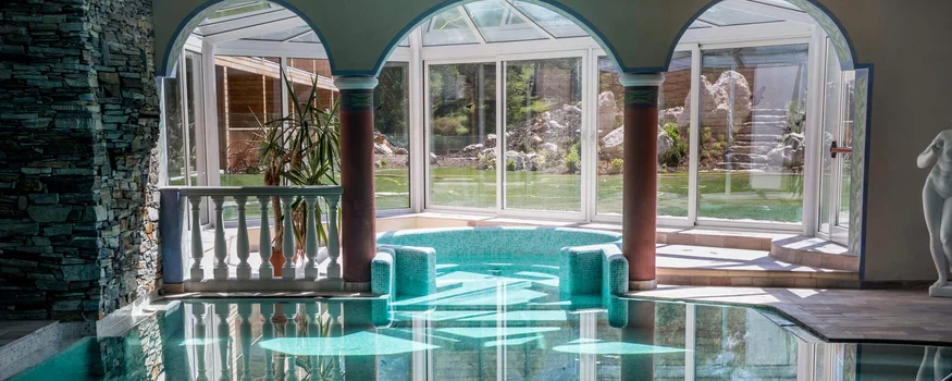 Indoor pool with columns, glass windows, and garden view outside