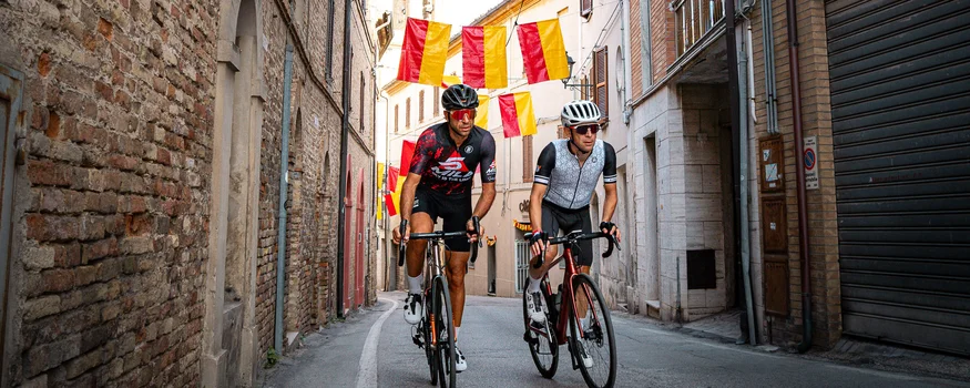 Zwei Radfahrer fahren durch eine Gasse mit rot-gelben Fahnen