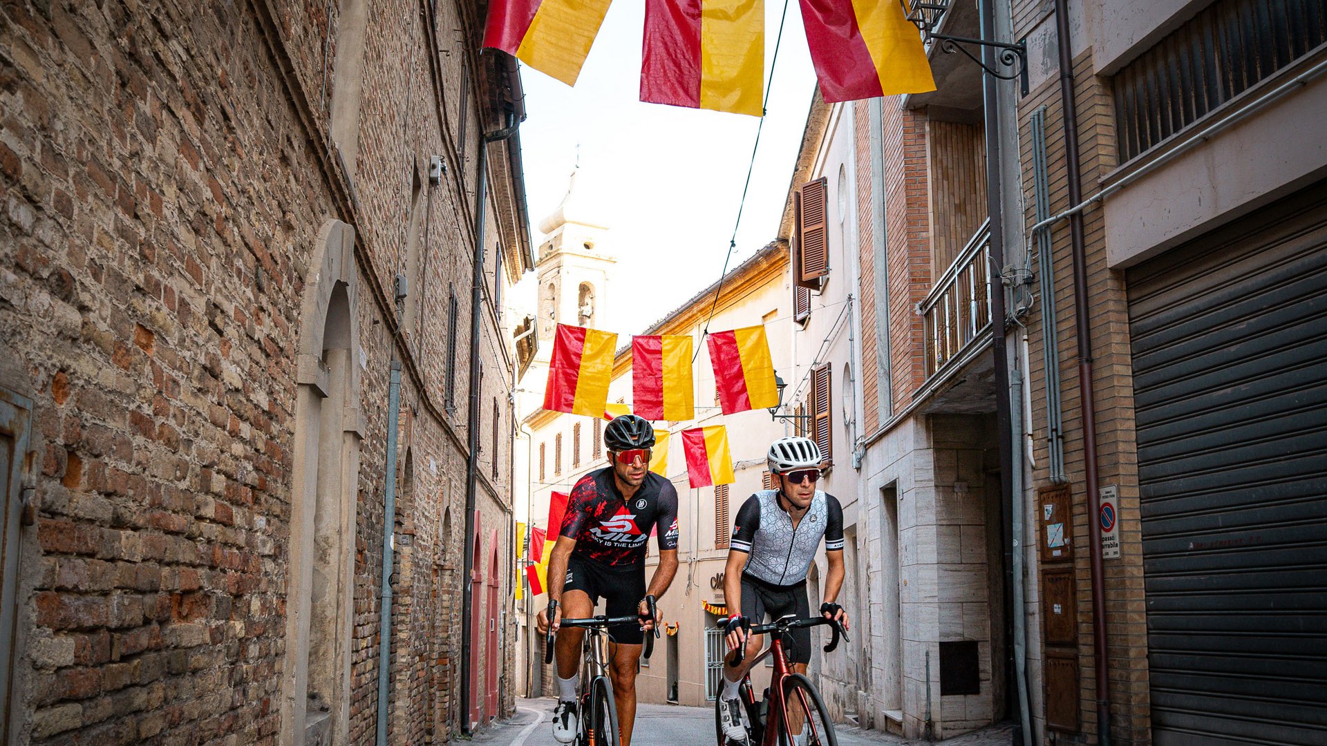 Zwei Radfahrer fahren durch eine Gasse mit rot-gelben Fahnen