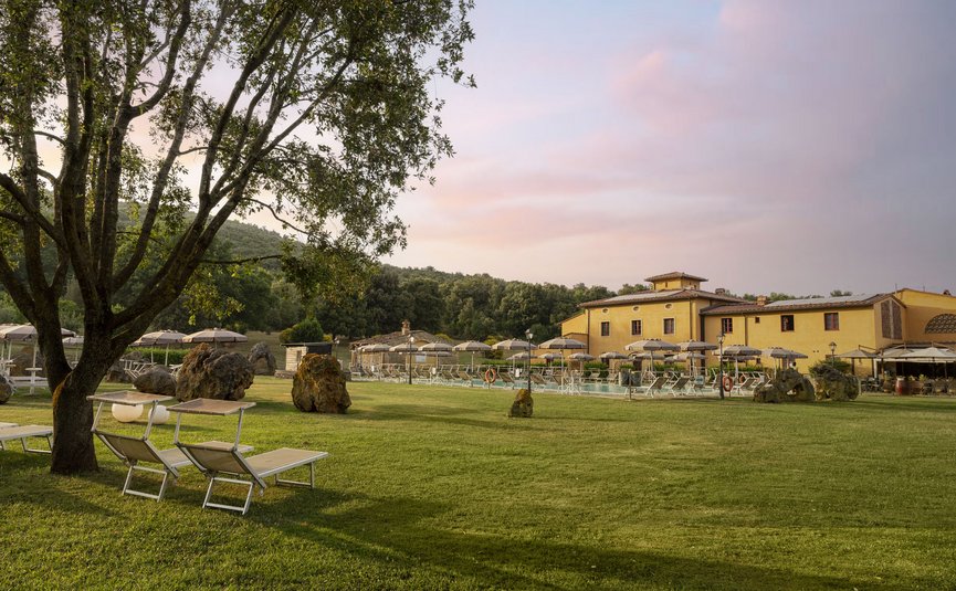 Hotel & Restaurant Casolare Le Terre Rosse ***S © Hotel Casolare Le Terre Rosse Grüner Garten mit Bäumen, Liegestühlen und Sonnenschirmen neben einem gelben Gebäude