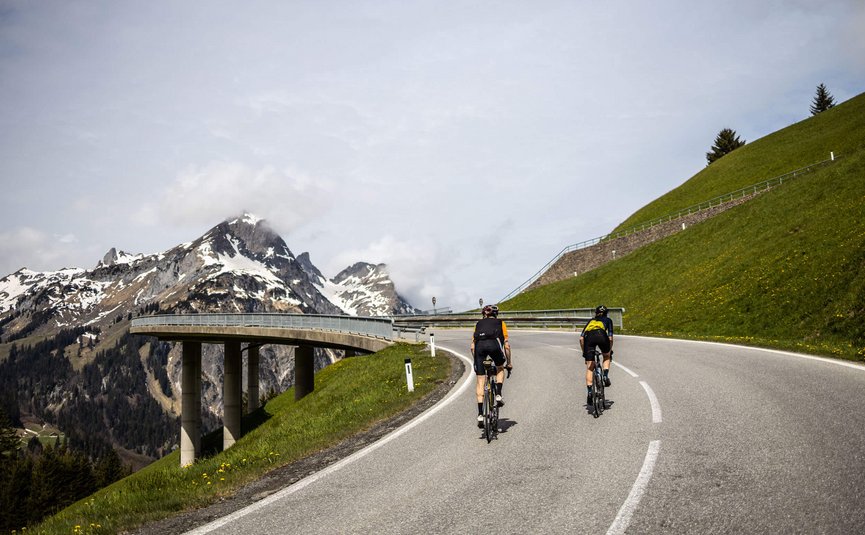 Due ciclisti su una strada di montagna con vette innevate sullo sfondo