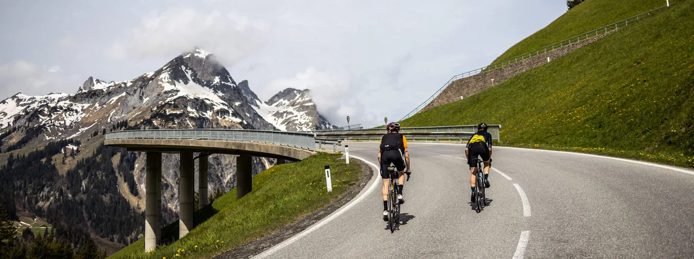 Passo Hochtannberg © Bregenzerwald Tourismus - Merlijn Spenkerlink Due ciclisti su una strada di montagna con vette innevate sullo sfondo