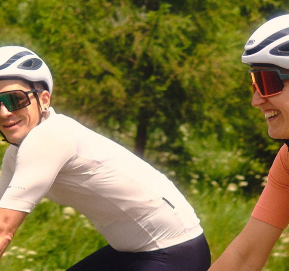 Zwei Radfahrer fahren auf einer Straße mit grüner Landschaft im Hintergrund