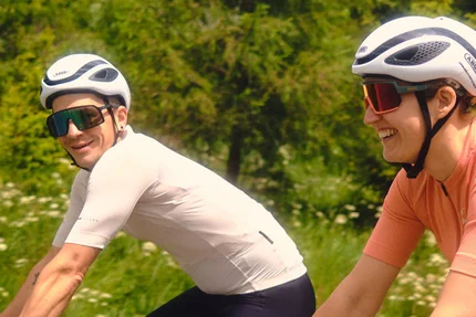 Zwei Radfahrer fahren auf einer Straße mit grüner Landschaft im Hintergrund