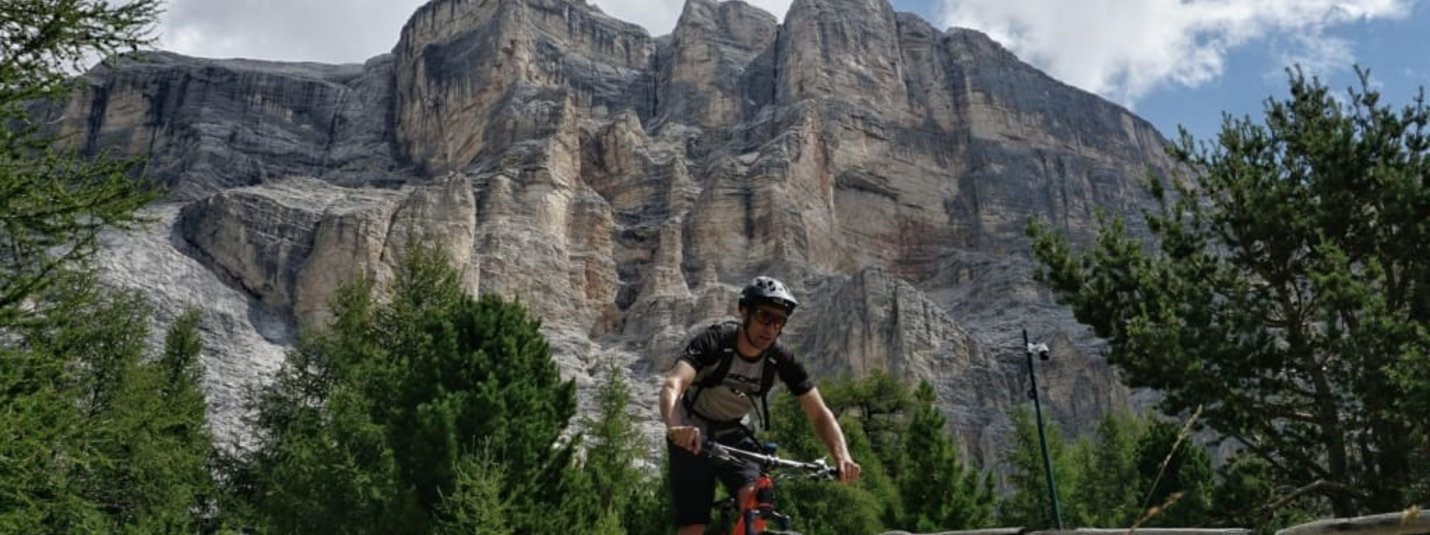 Mountainbiker fährt auf einem Waldweg vor hohen Felsen und bewölktem Himmel