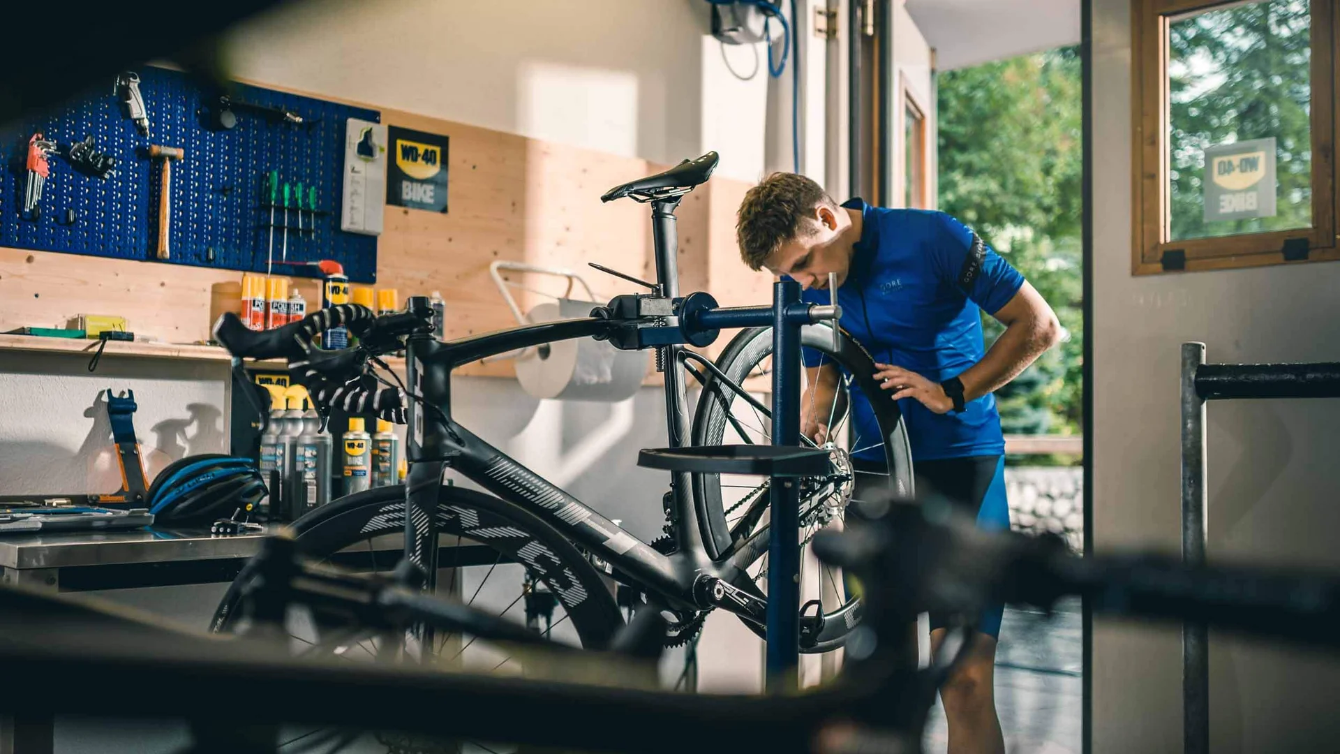 Bicycle mechanic repairing road bike in workshop with tools on wall