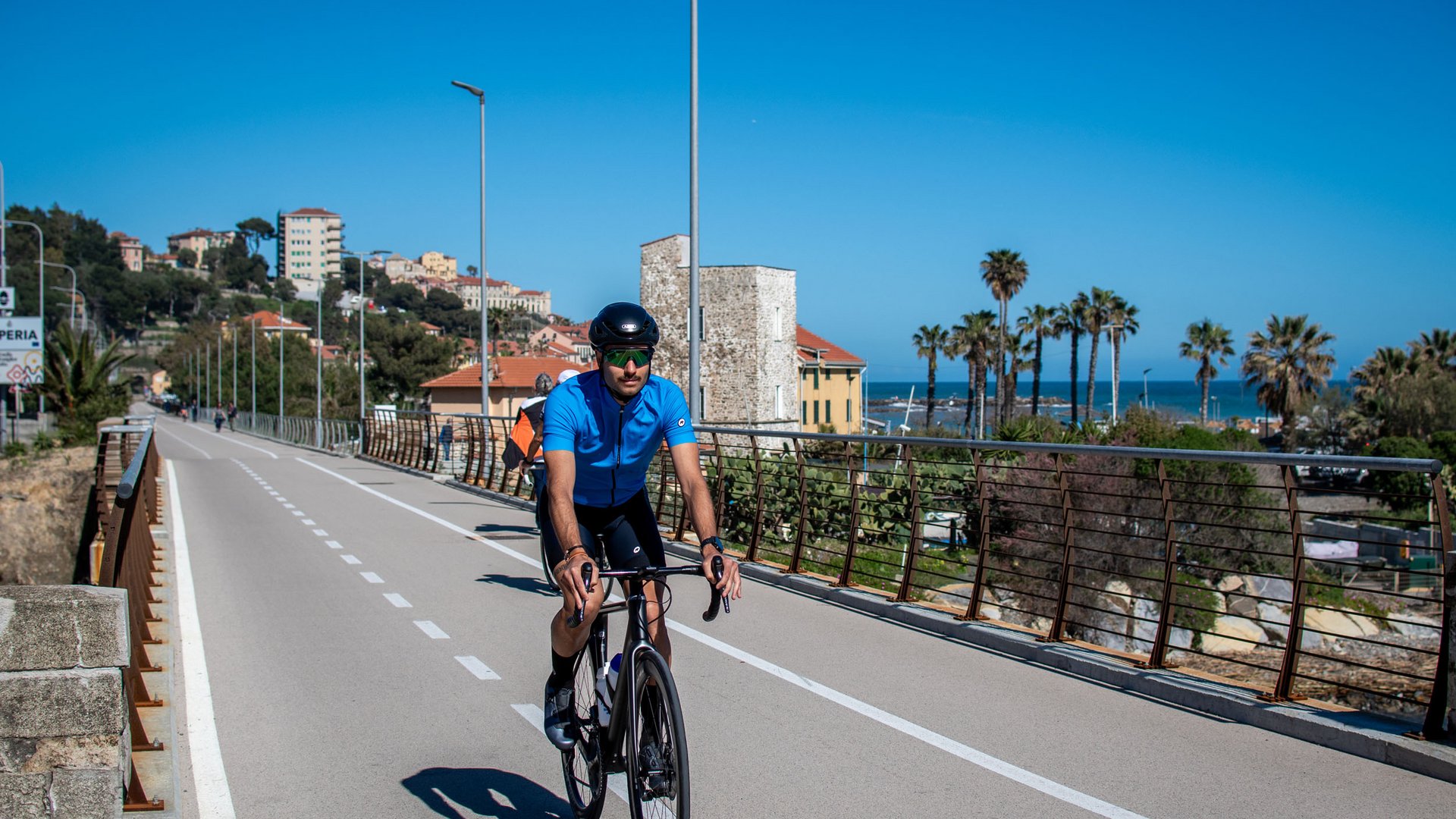 Radfahrer auf Küstenweg bei klarem Himmel und Palmen im Hintergrund