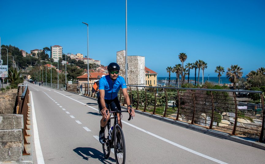 Cyclist on coastal path with clear sky and palm trees in background