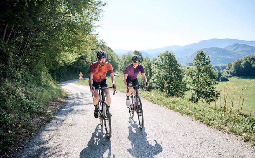 Due ciclisti su una strada di campagna con colline boschive sullo sfondo