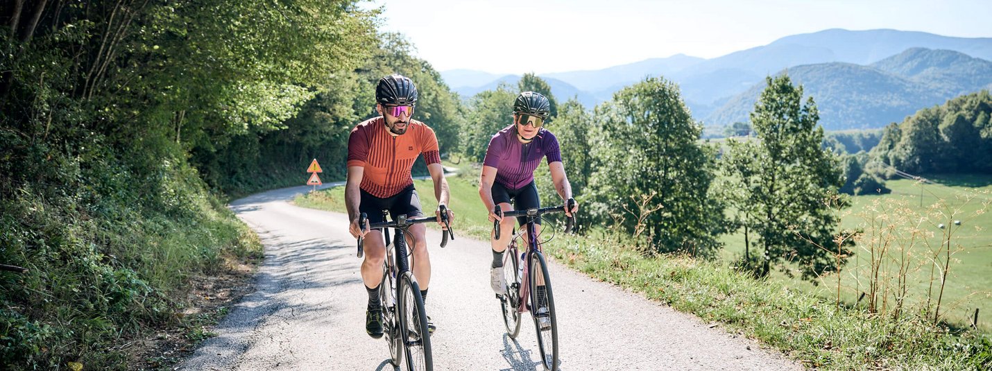 Due ciclisti su una strada di campagna con colline boschive sullo sfondo