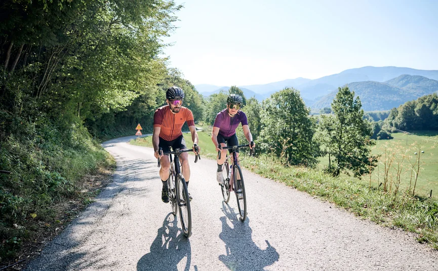 Due ciclisti su una strada di campagna con colline boschive sullo sfondo