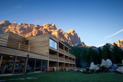 Modern wooden building with sunlit mountains and forest in the evening light