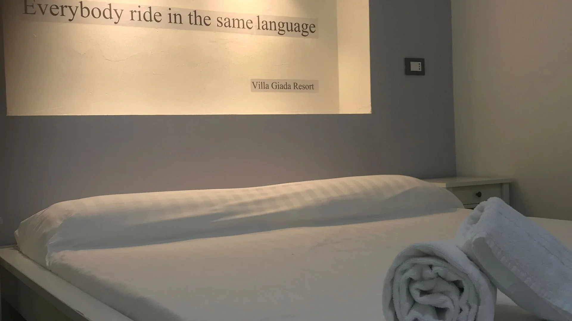 Villa Giada SpEace Resort: Mit deinem Rennrad aufs Zimmer © Villa Giada spEace Resort Weißes Bett mit gerollten Handtüchern und Schriftzug an der Wand