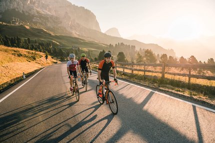 Three cyclists riding on a mountain road at sunset