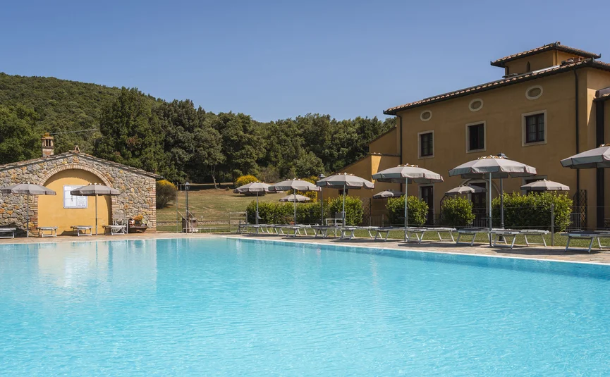 Pool mit Sonnenschirmen und Liegestühlen vor einem Haus in ländlicher Umgebung