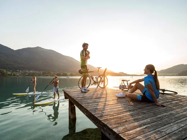 Ein Rennrad-Wochenende im SalzburgerLand – Salzkammergut © Markus Greber Personen auf Steg und Stand-up-Paddle-Boards bei Sonnenuntergang am See