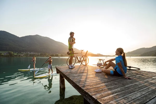 Mensen op steiger en paddleboards bij zonsondergang op het meer