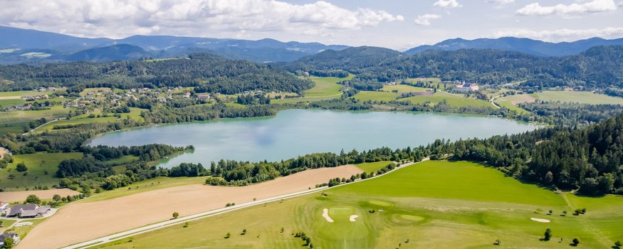 Bed&Breakfast Mittelkärnten © Michael Stabentheiner - Region Mittelkärnten Aerial view of green golf course beside a lake and mountains in the background