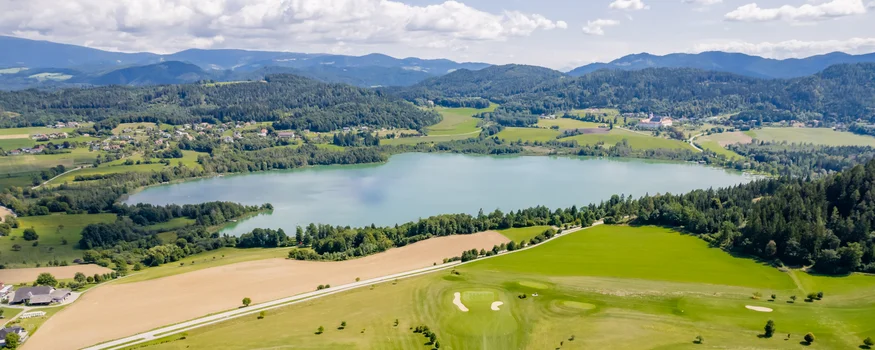 Aerial view of green golf course beside a lake and mountains in the background