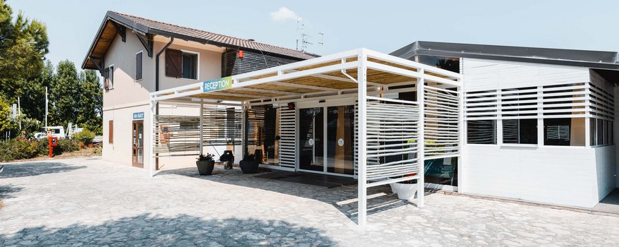 Empfangsbereich eines hellen Gebäudes mit überdachtem Eingang und Empfangsschild