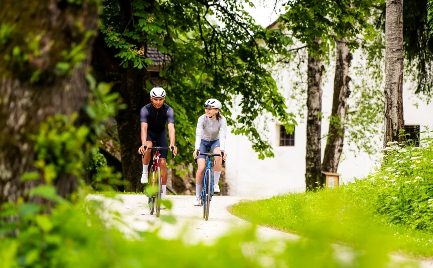 Zwei Radfahrer fahren auf einem Weg umgeben von Bäumen und Wiesen