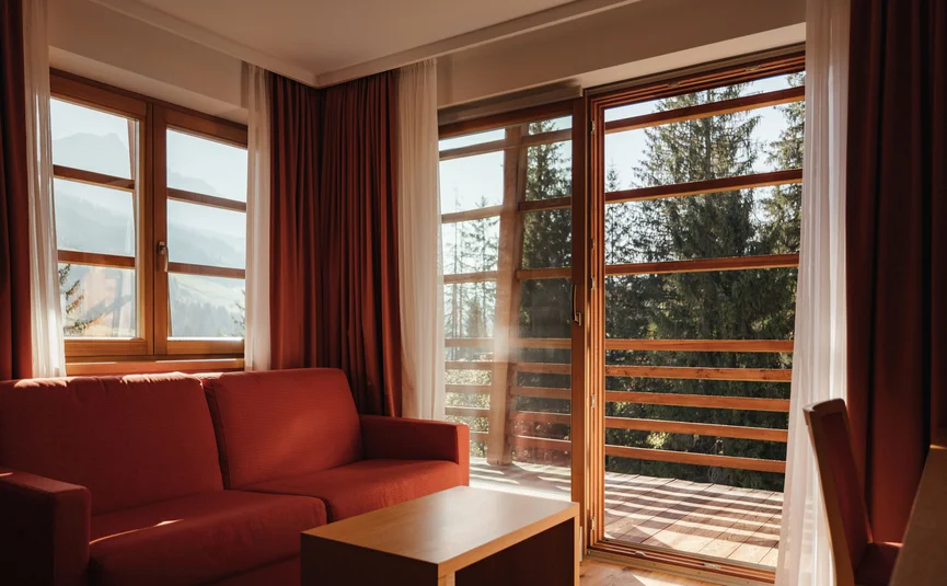 Divano rosso e tavolo in legno vicino a grandi finestre con vista su foresta e montagne