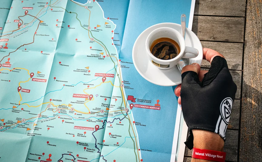 Hand mit Handschuh hält Espresso über einer Landkarte auf Holztisch