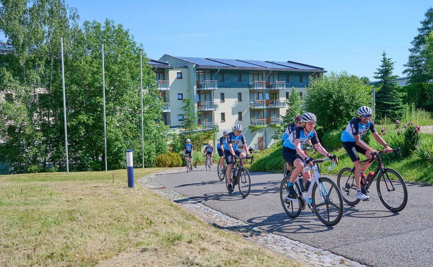 Gruppo di ciclisti su un sentiero soleggiato vicino a edifici moderni