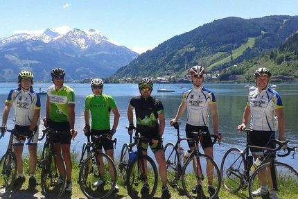Sei ciclisti con bici da corsa davanti a un lago di montagna con cime innevate
