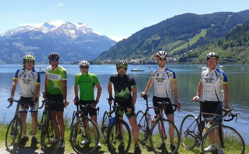 Sei ciclisti con bici da corsa davanti a un lago di montagna con cime innevate