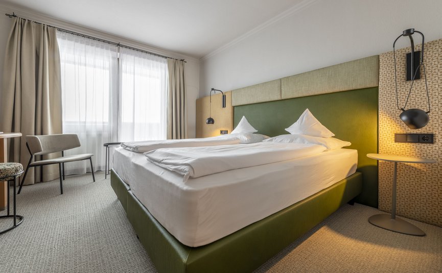 Bright hotel room with green bed and two hanging lamps beside a small table