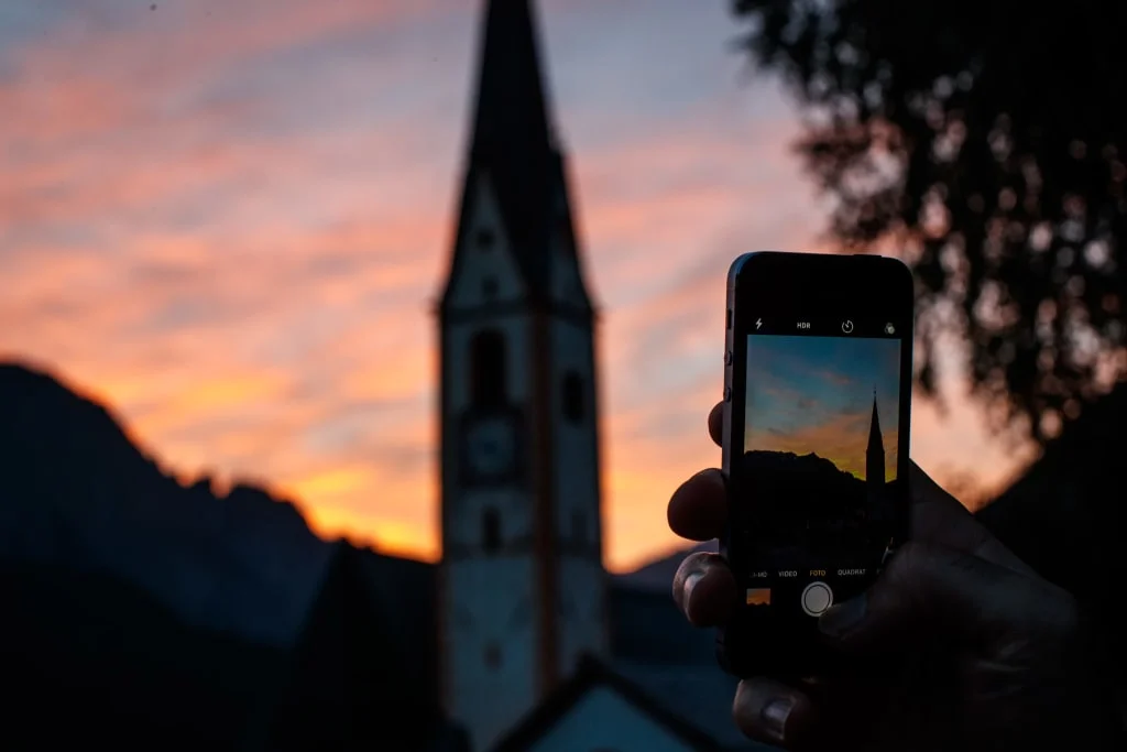 Hand hält Smartphone und fotografiert Kirchturm bei Sonnenuntergang