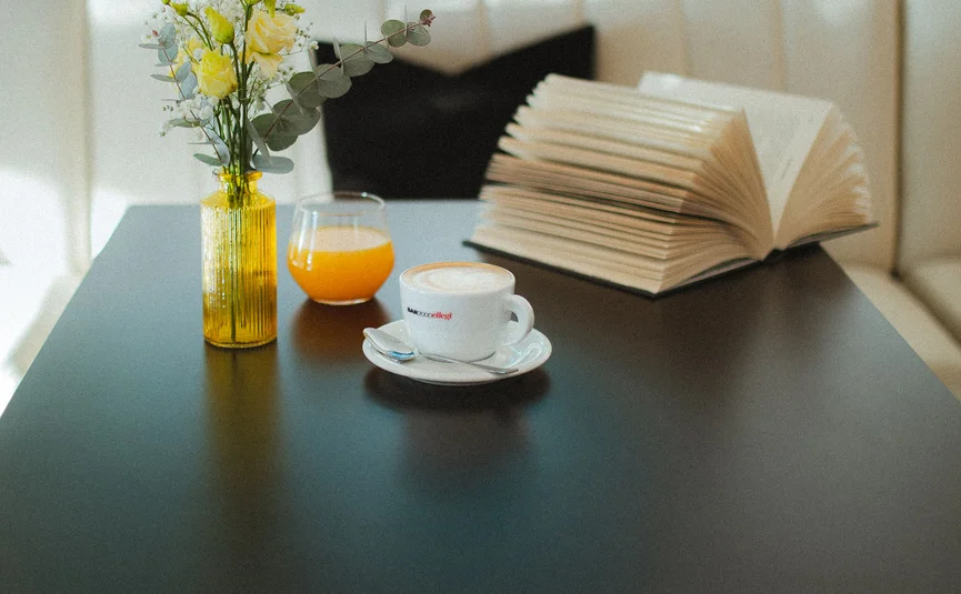 Hotel Capris **** © Hotel Capris Capodistria Boutique Zwart tafel met gele vaas, sinaasappelsap, koffie en een open boek