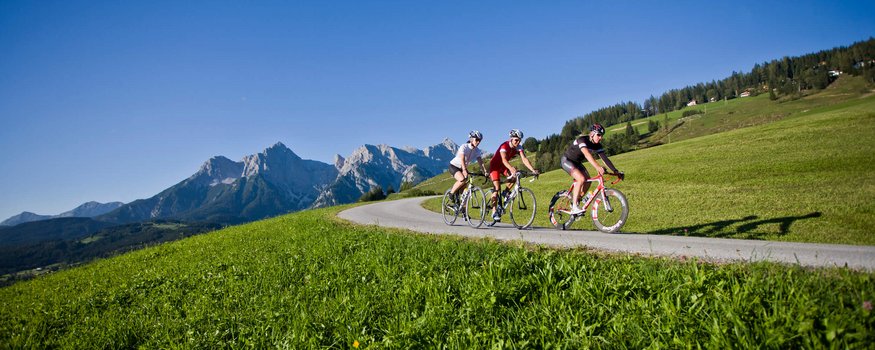 Pinzgau © Heiko Mandl Drei Radfahrer fahren auf bergiger Straße mit Bergen im Hintergrund