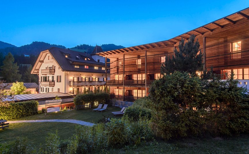 Beleuchtete Hotels mit Garten und Liegestühlen bei Abenddämmerung in den Bergen