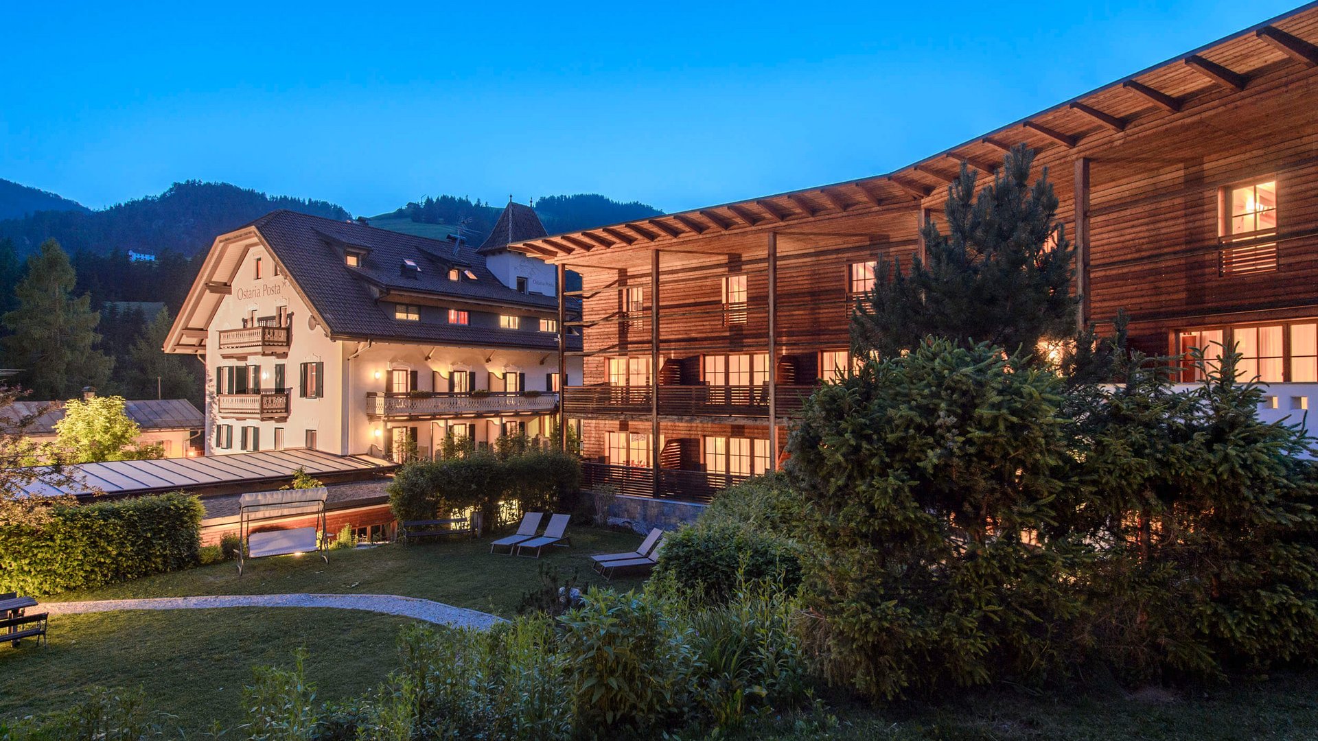 Beleuchtete Hotels mit Garten und Liegestühlen bei Abenddämmerung in den Bergen